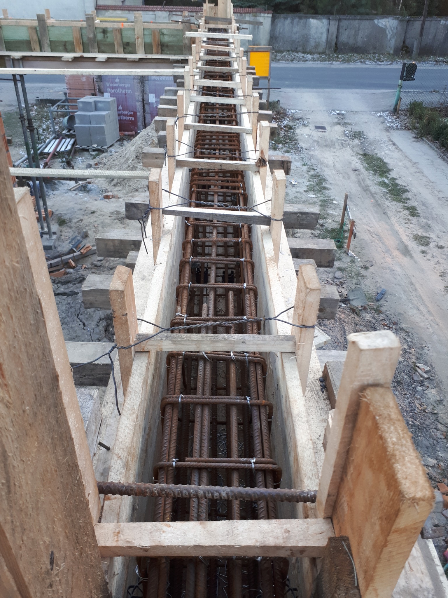 Szalunek zbrojeniowy pod wylewkę, widok z góry na stalowe pręty w drewnianej konstrukcji, w tle bloczki betonowe i droga.