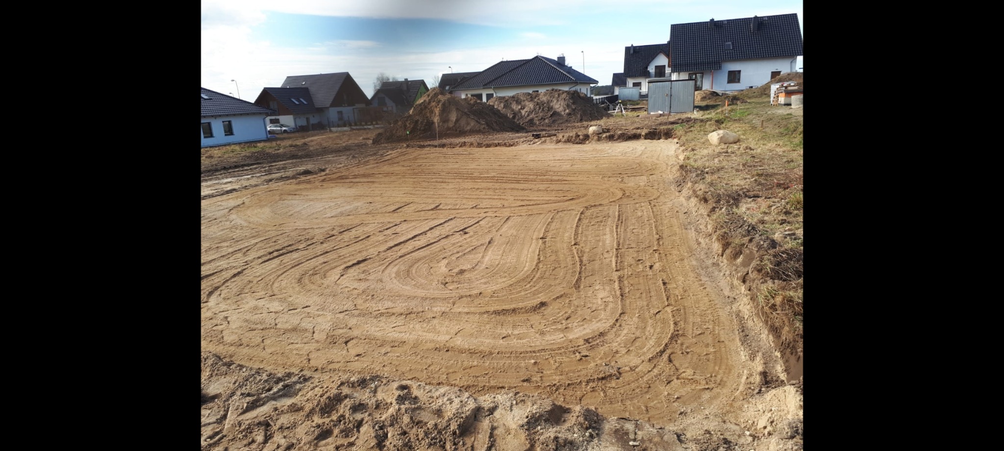 Przygotowany teren pod budowę domu z widocznymi śladami po maszynach, w tle zabudowa jednorodzinna.