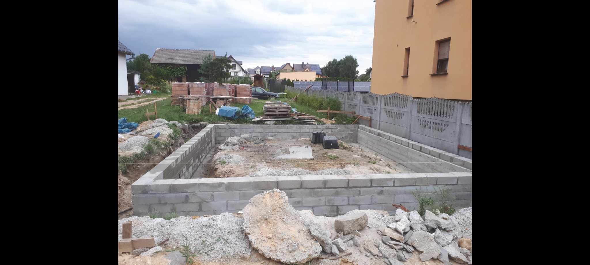 Budowa fundamentów garażu dwustanowiskowego: wylany betonowy fundament obłożony bloczkami betonowymi, widoczne materiały budowlane i otoczenie placu budowy.