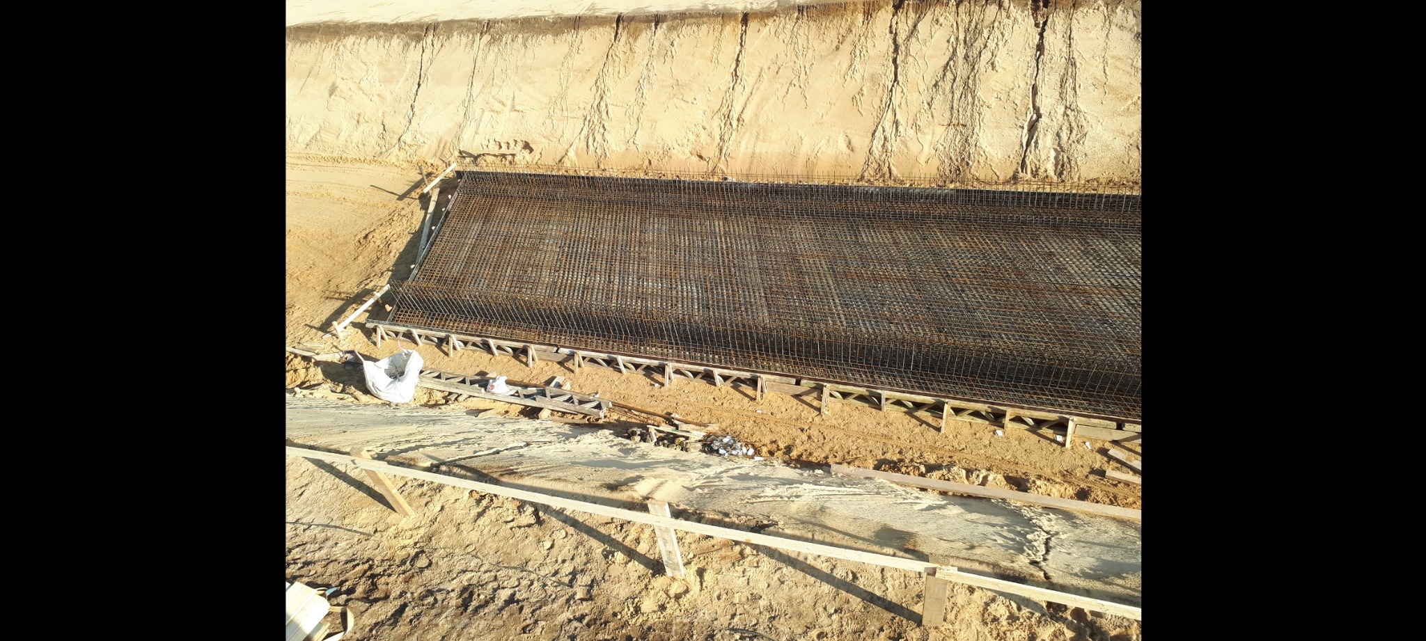 Przygotowanie zbrojenia na gruncie pod płytę fundamentową, widok z góry na wykop z drewnianym szalunkiem.