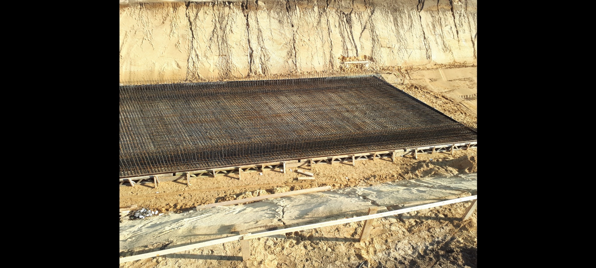 Zbrojenie płyty fundamentowej ułożone na drewnianych podporach, widok z góry na wykop z ziemi.