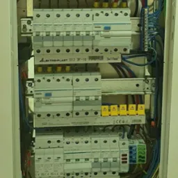 Rozdzielnica elektryczna w białej obudowie, widoczne zabezpieczenia, przewody i listwy zaciskowe. Instalacja połączona, gotowa do użytku.