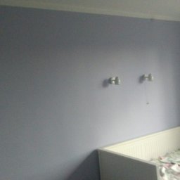 Adam Wykonczenia - Świeżo pomalowany pokój dziecięcy w odcieniach fioletu z dwoma kinkietami nad łóżeczkiem dziecięcym z białymi szczebelkami.