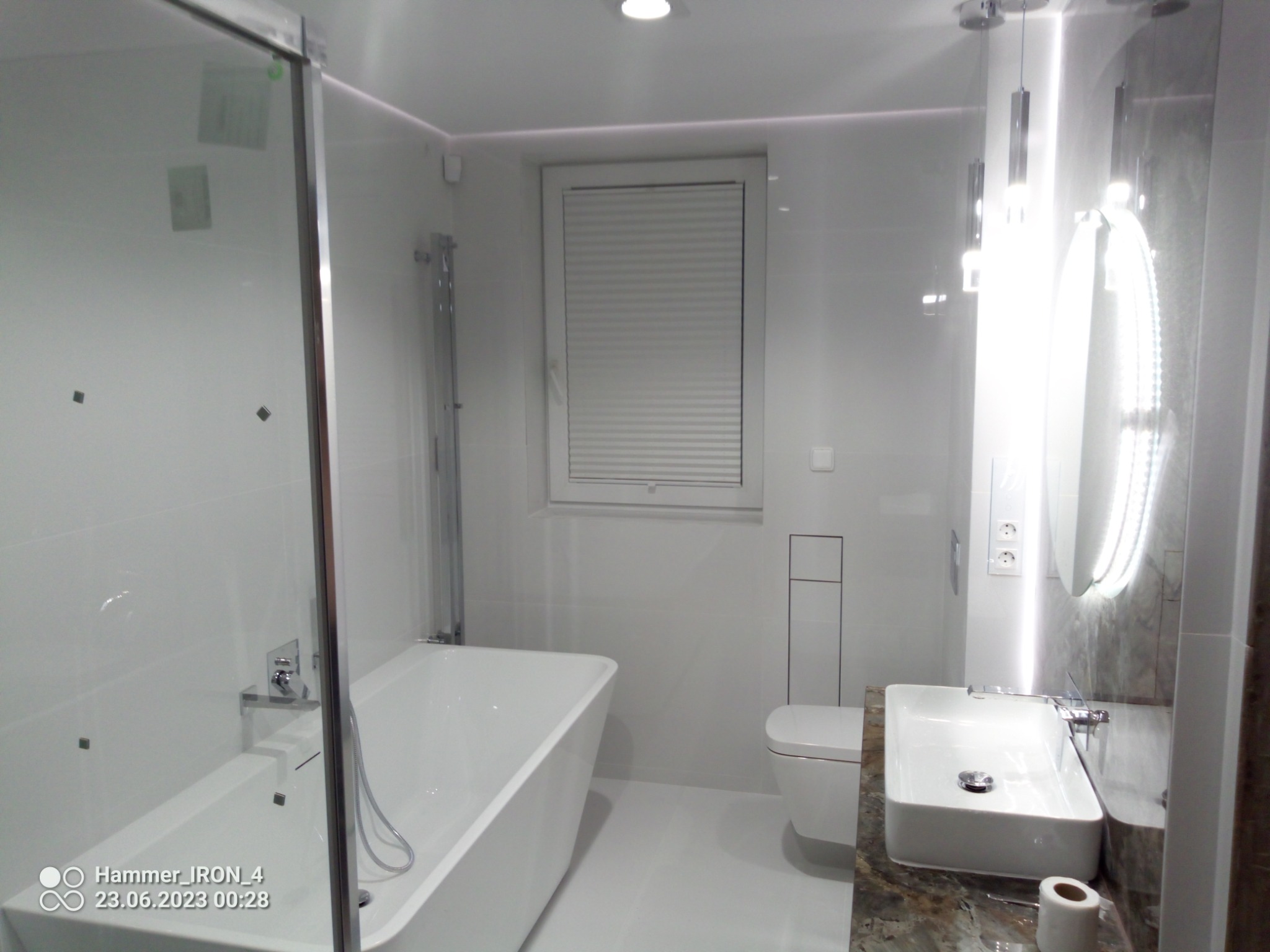 Nowoczesna, minimalistyczna łazienka po remoncie z białą armaturą, przeszkloną kabiną prysznicową, podświetlanym lustrem i marmurowym blatem pod umywalką.