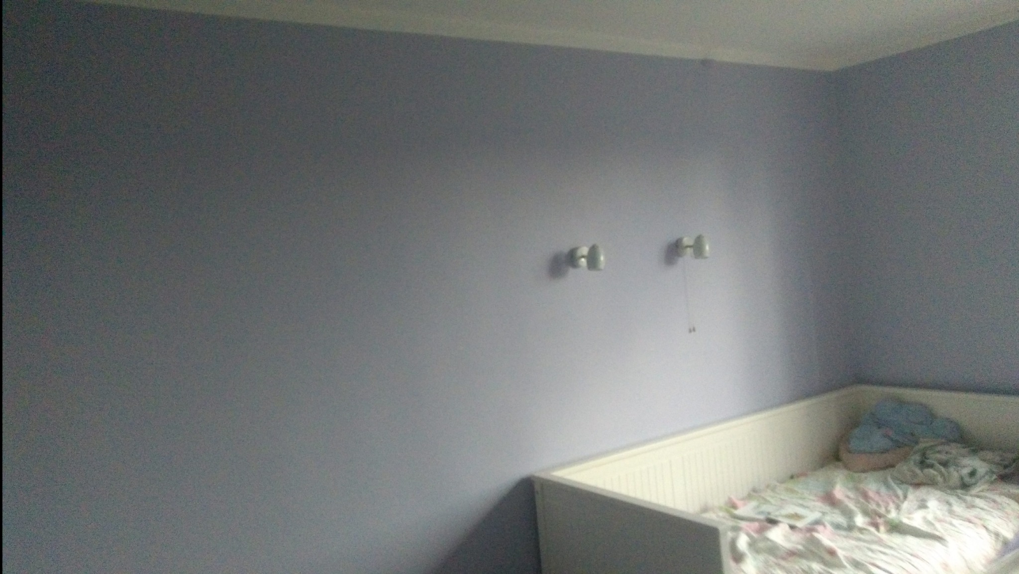 Świeżo pomalowany pokój dziecięcy w odcieniach fioletu z dwoma kinkietami nad łóżeczkiem dziecięcym z białymi szczebelkami.