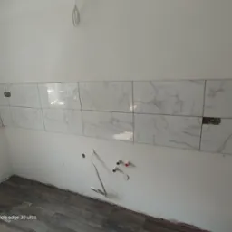 Fragment ściany w trakcie układania płytek imitujących marmur w kuchni. Widoczne otwory na gniazdka i instalację wodną, podłoga wyłożona panelami.