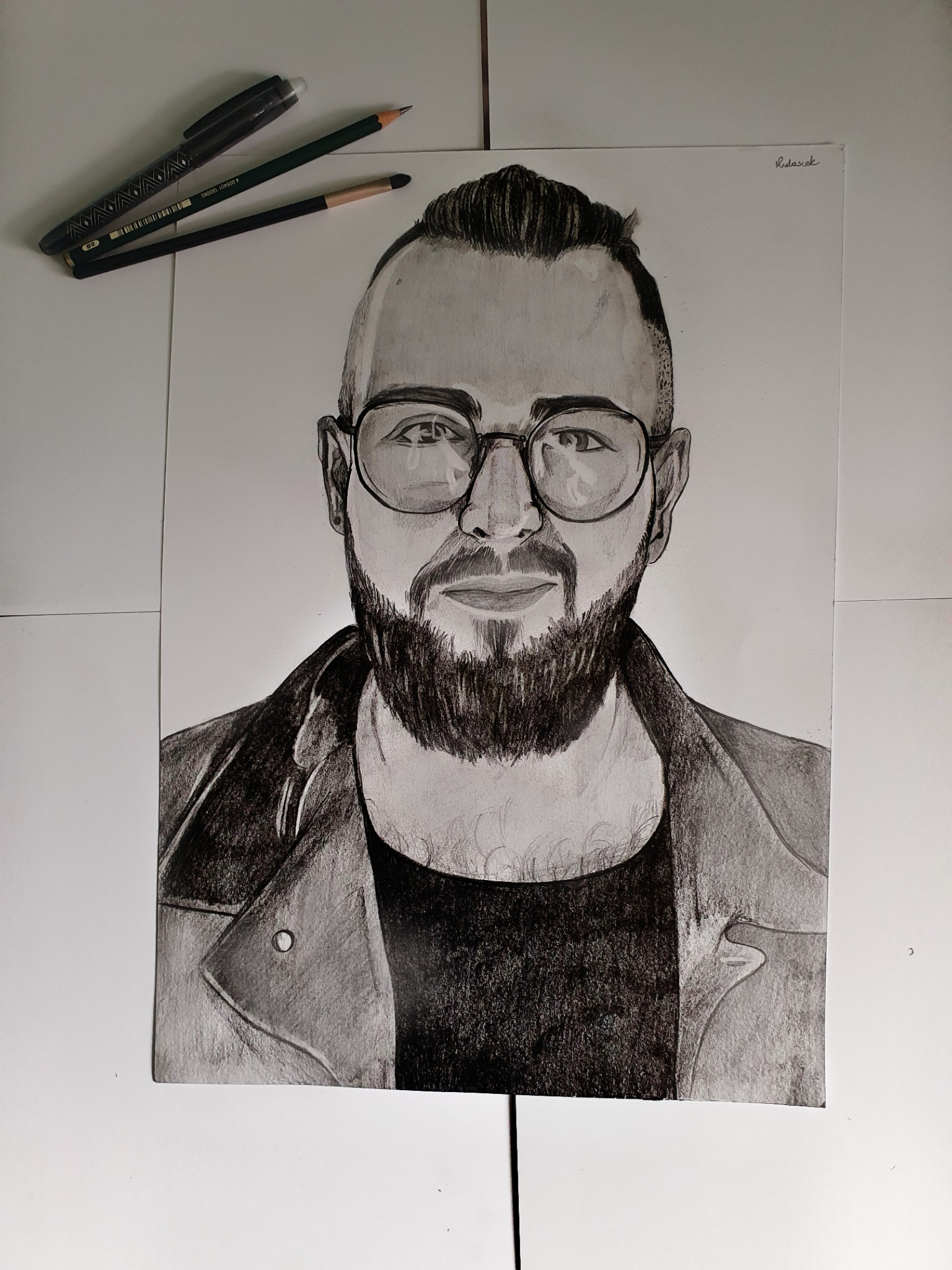 Ręcznie rysowany portret mężczyzny w okularach, format A4, obok leżą ołówki i cienkopis.