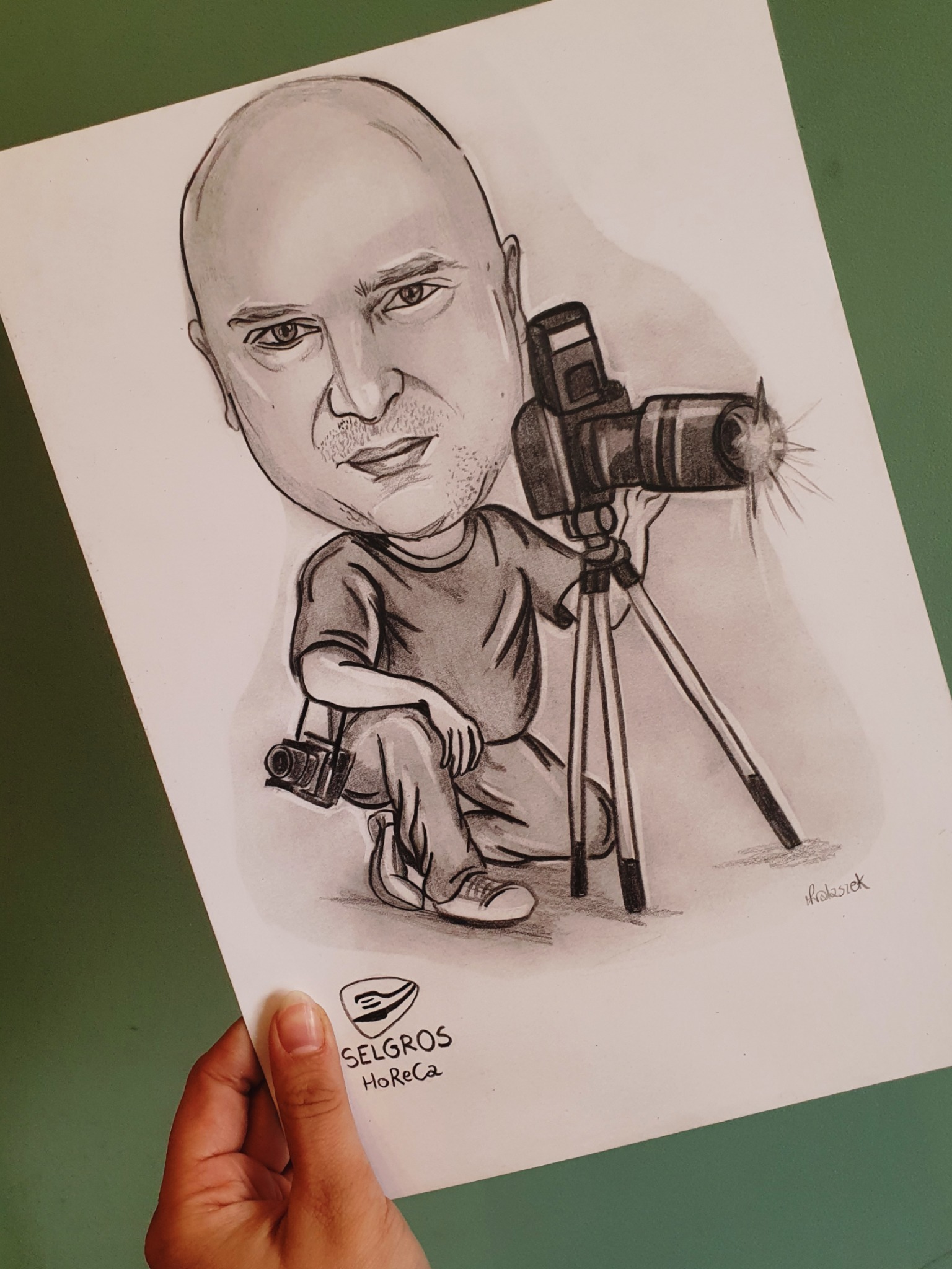 Ręcznie rysowana karykatura mężczyzny z aparatem na statywie, trzymana w dłoni, z widocznym logo Selgros HoReCa w dolnym rogu.