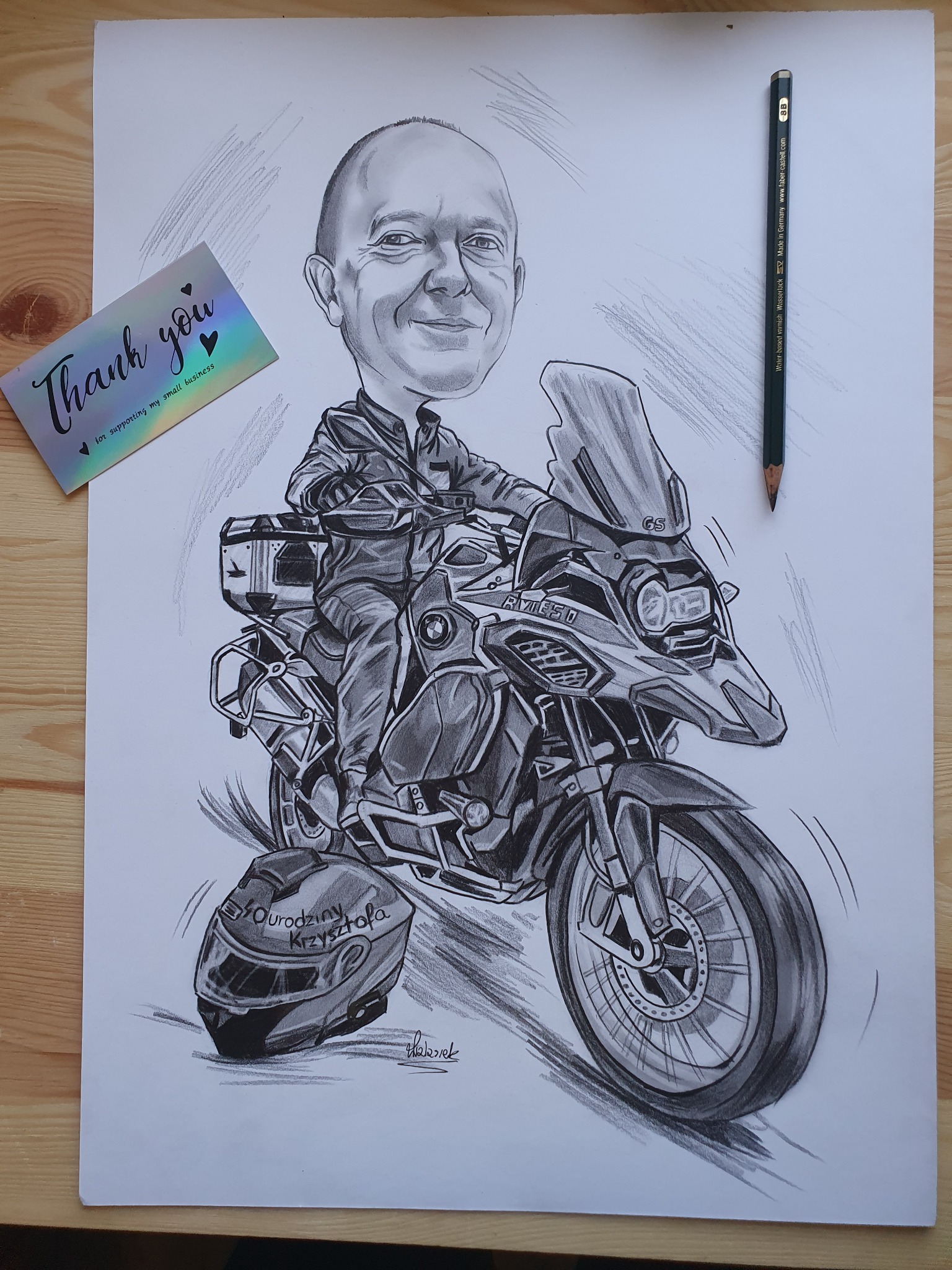 Ręcznie rysowany portret karykaturalny mężczyzny na motocyklu BMW R1250 GS, z kaskiem z napisem 'Urodziny Krzysztofa', leżącym obok. Obok leży ołówek.