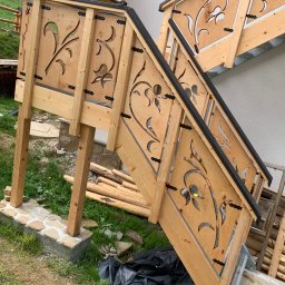Zubek Frez CNC - Zewnętrzne schody drewniane z ozdobnymi wycięciami w balustradach, czarne elementy wykończeniowe, częściowo wykonane, widoczne materiały budowlane obok.