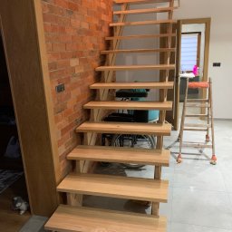 Zubek Frez CNC - Surowe, drewniane stopnie schodów przy ceglanej ścianie, widoczna drabina malarska i wózek inwalidzki w tle.