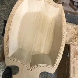 Drewniana misa dekoracyjna w trakcie obróbki, widoczne detale wykończenia krawędzi, surowe drewno, warsztat stolarski w tle.