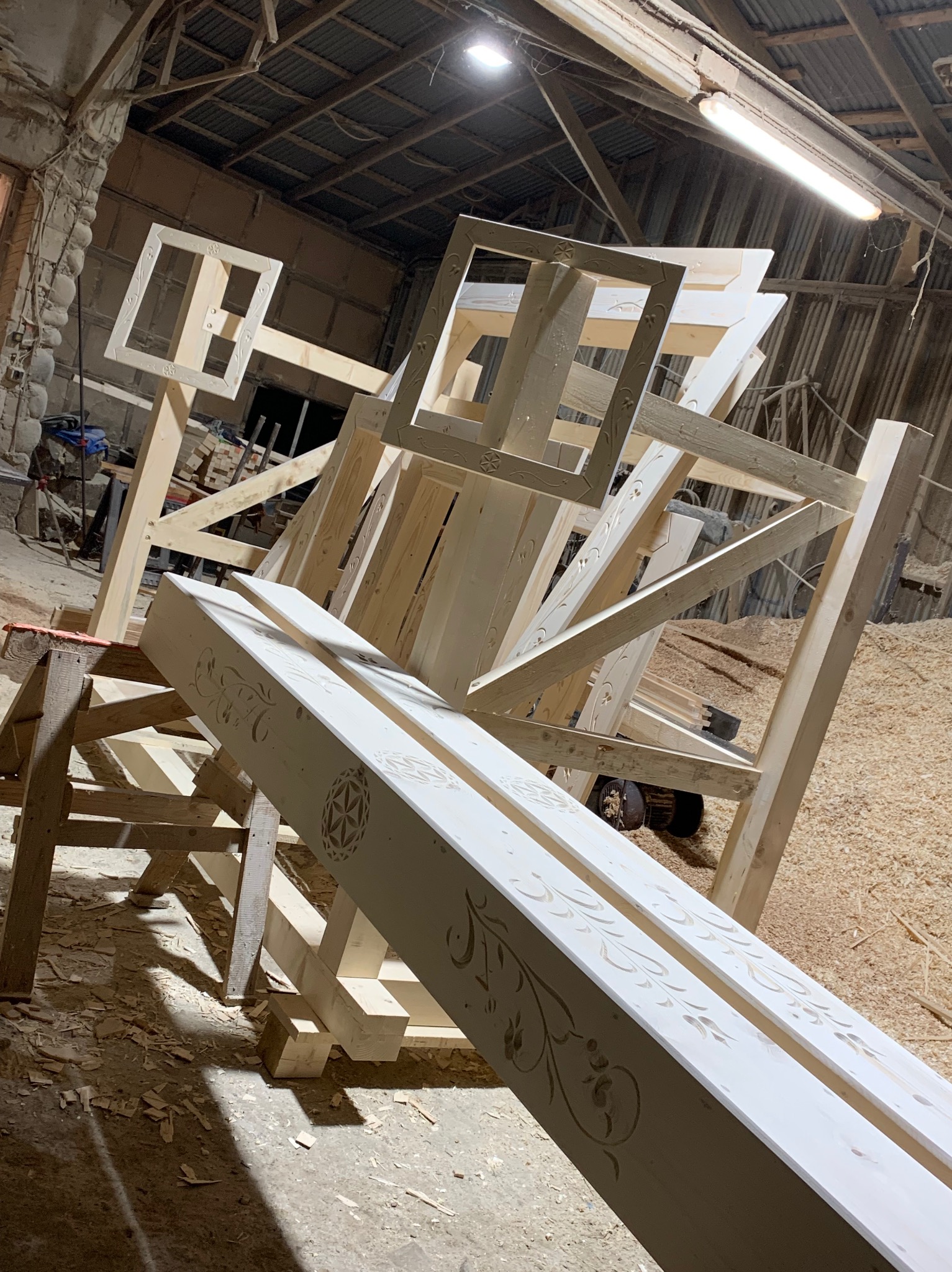 Wykonywanie drewnianych elementów dekoracyjnych z wyfrezowanymi wzorami w warsztacie stolarskim, widoczne drewniane konstrukcje i stół roboczy.