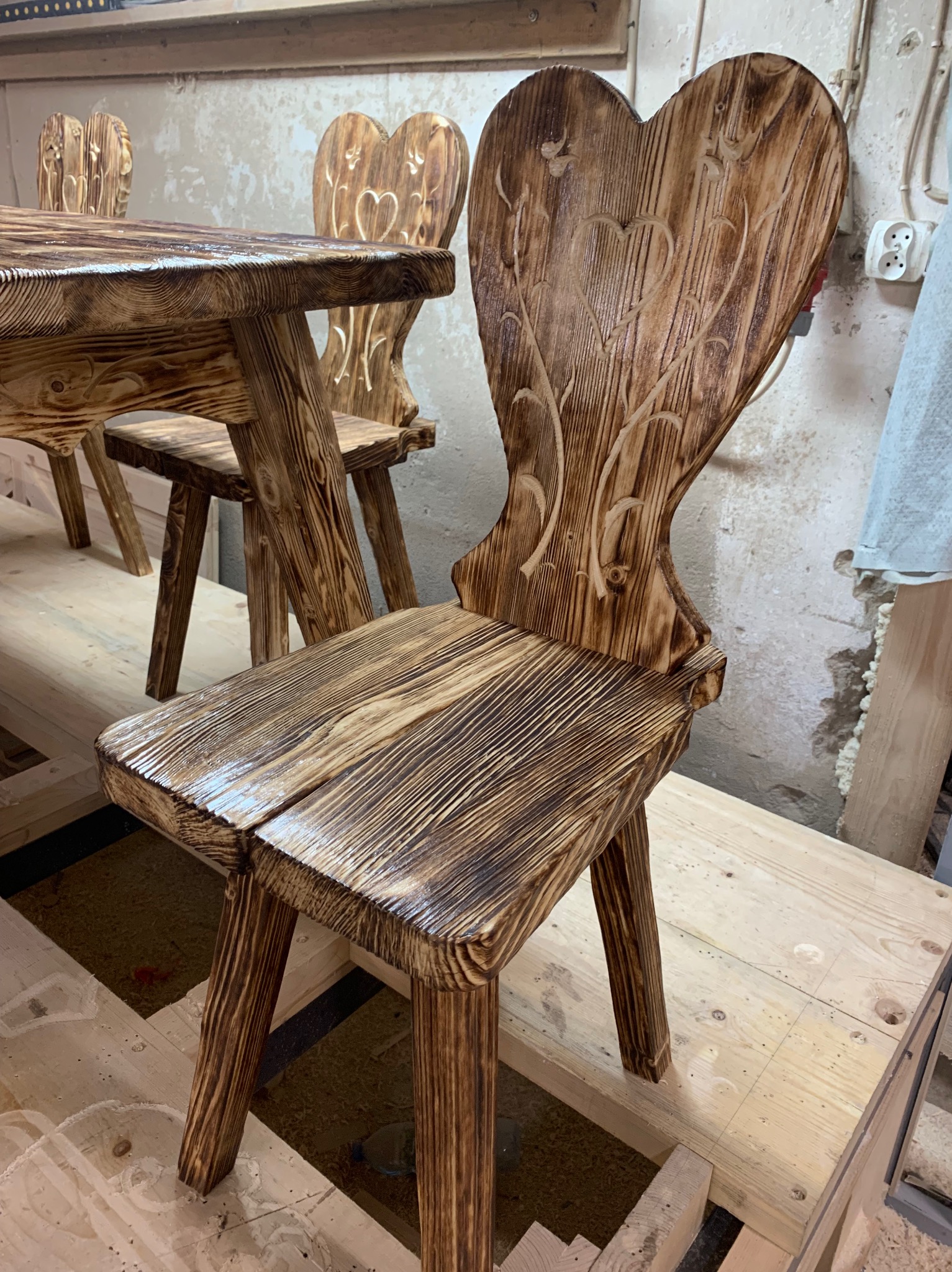 Ręcznie robione, opalane krzesło z drewna z wyciętym wzorem serca na oparciu, widoczne w Maruszynie, część kompletu ze stołem.