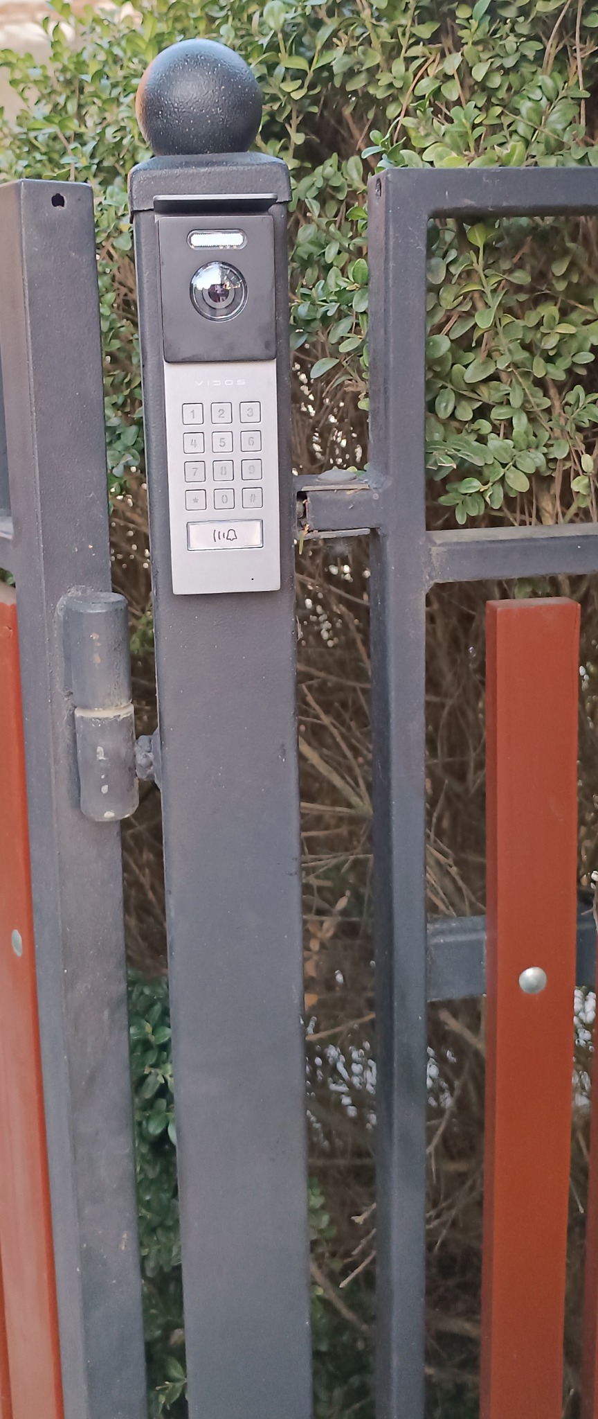 Szary wideodomofon z klawiaturą numeryczną zamontowany na metalowej bramie w Pruszkowie, widok z bliska.