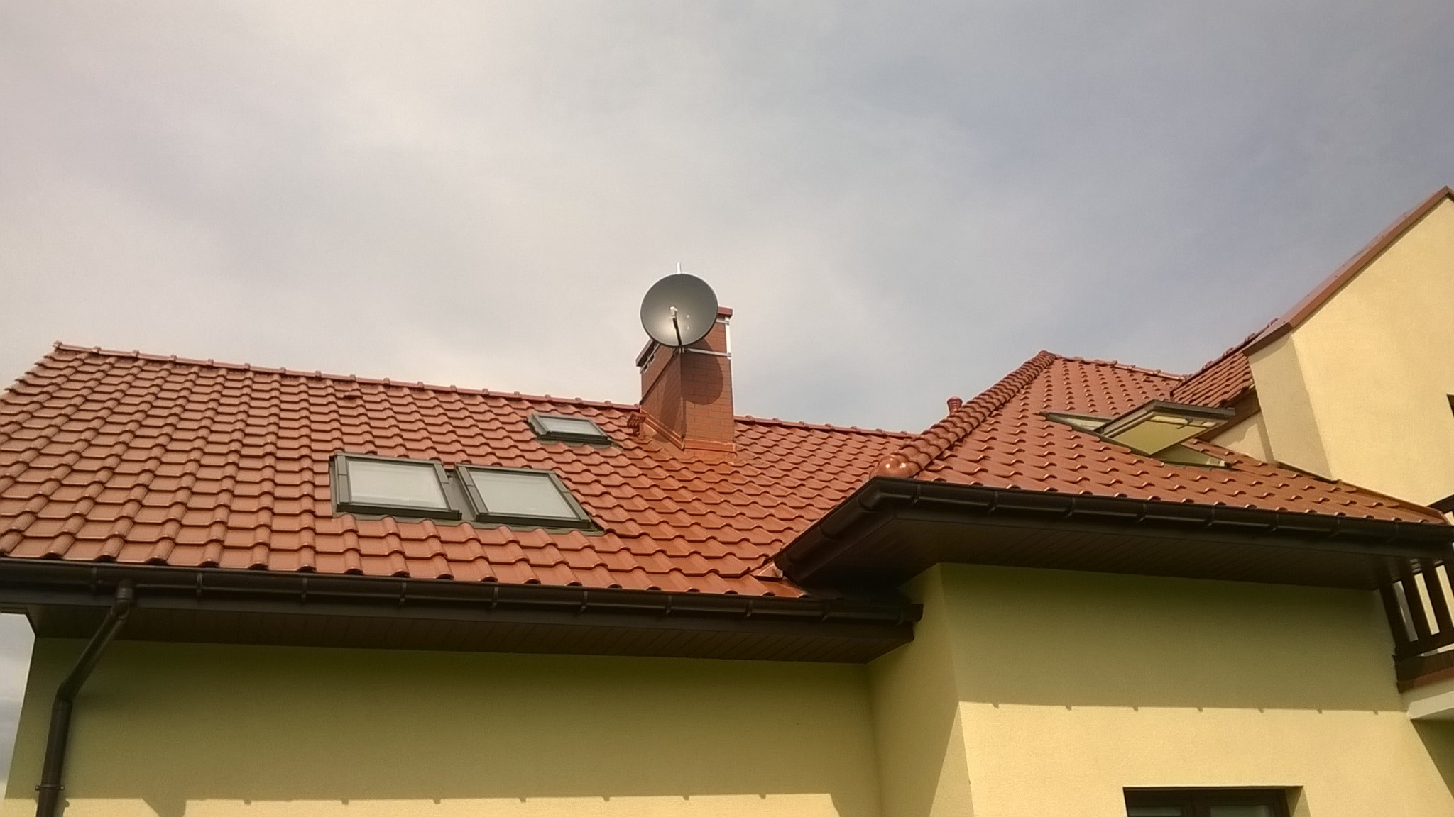 Antena satelitarna zamontowana na kominie domu z czerwoną dachówką i oknami dachowymi.