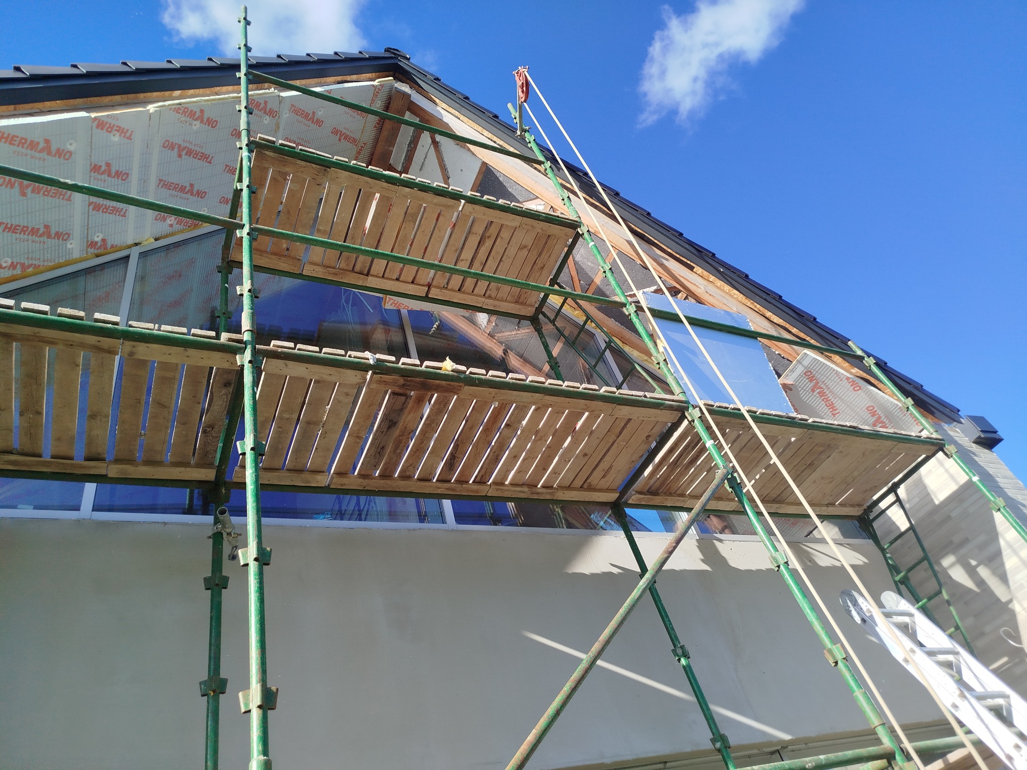 Ocieplanie poddasza domu jednorodzinnego z użyciem rusztowania. Widoczne płyty termoizolacyjne THERMANO i fragment nieba.