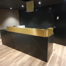 Recepcja z czarnego marmuru z złotym blatem, widoczne fragmenty wykończenia wnętrza.