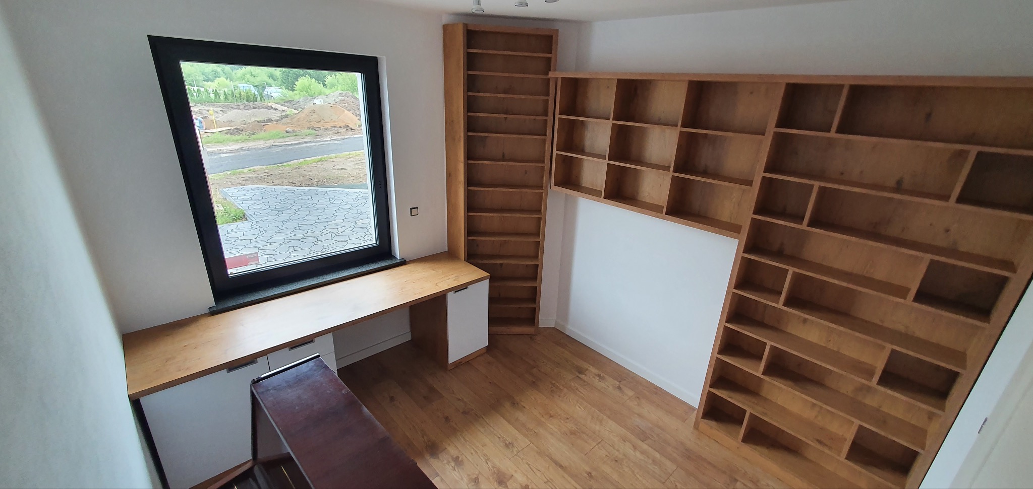 Drewniane regały na książki i biurko pod oknem w nowoczesnym wnętrzu, jasne drewno, białe fronty szafek, widok z góry.