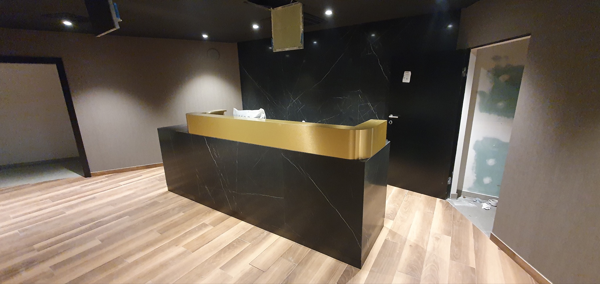 Recepcja z czarnego marmuru z złotym blatem, widoczne fragmenty wykończenia wnętrza.