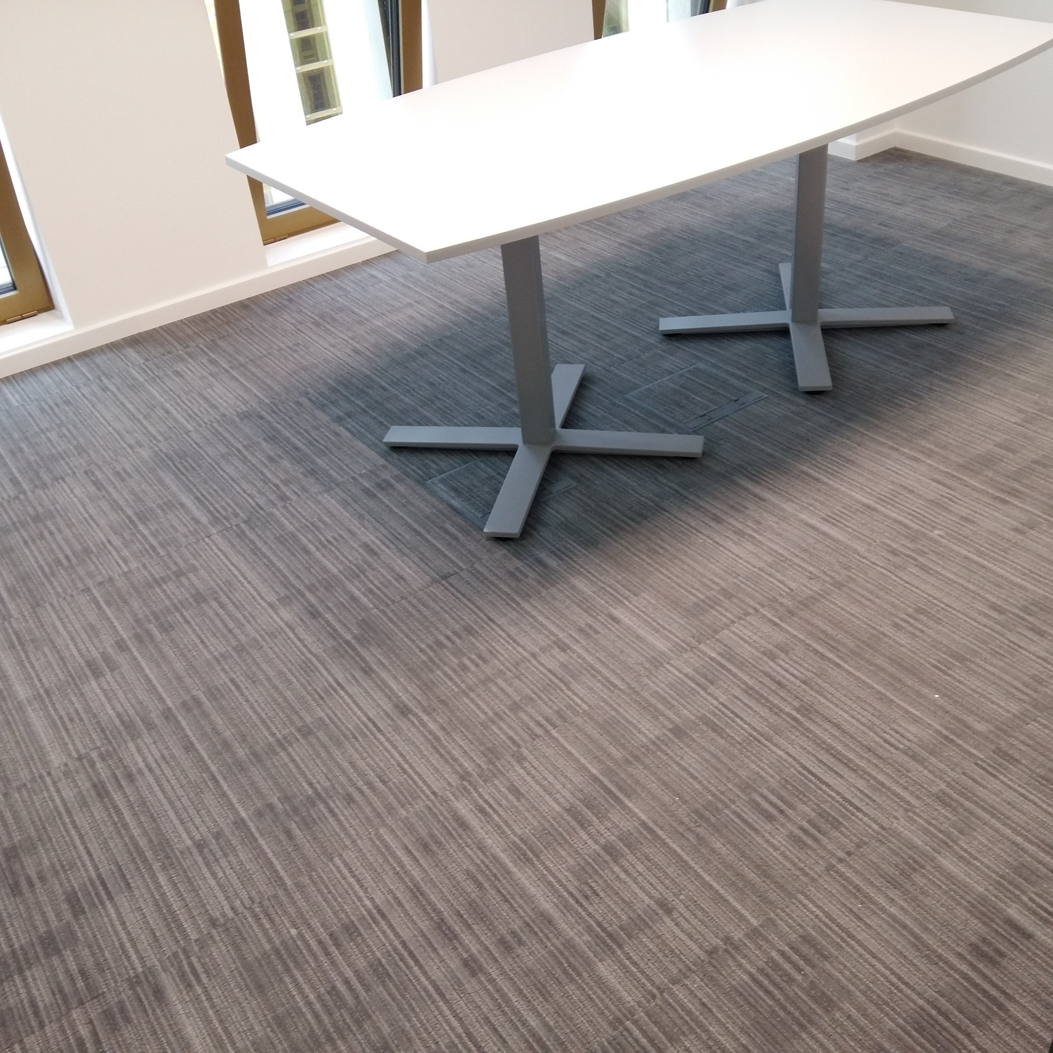 Szara wykładzina dywanowa w biurze, widoczny fragment białego biurka na metalowej podstawie.