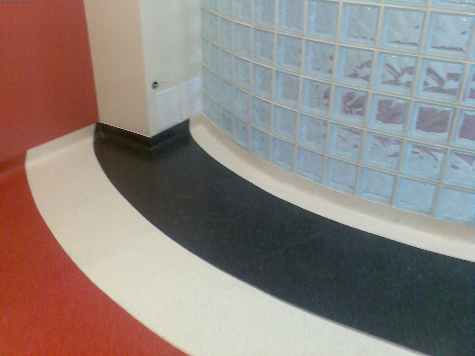 Zakrzywiona ściana z luksferów w łazience z wykończoną podłogą w kolorach czerwieni, bieli i czerni.