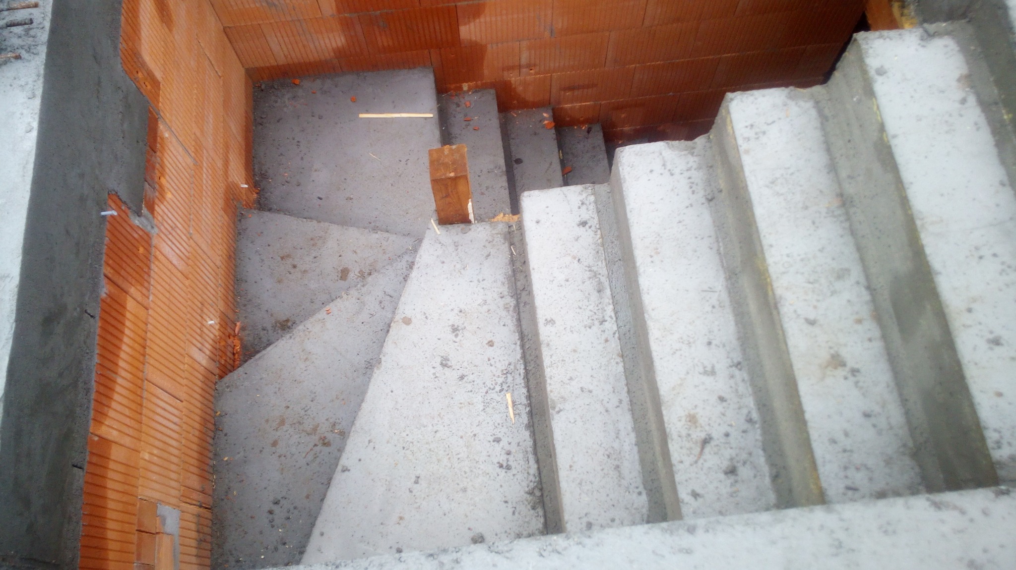 Wewnętrzne, betonowe schody spiralne w surowym stanie, z widoczną konstrukcją z czerwonej cegły dziurawki po bokach i drewnianymi elementami szalunku.