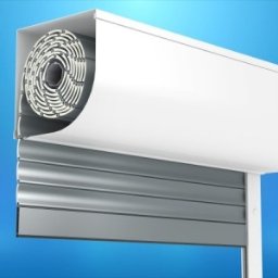 ALMAR DI - Przekrój przez zwiniętą roletę zewnętrzną z widocznym mechanizmem i aluminiowymi lamelami, na jednolitym niebieskim tle.