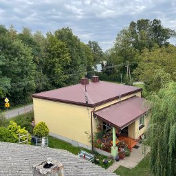 PAN OD DACHÓW SZYMON BIAŁECKI - Dom jednorodzinny z nowym, bordowym dachem widziany z góry, z widoczną starą dachówką na pierwszym planie i pracującym robotnikiem przy elewacji w tle.