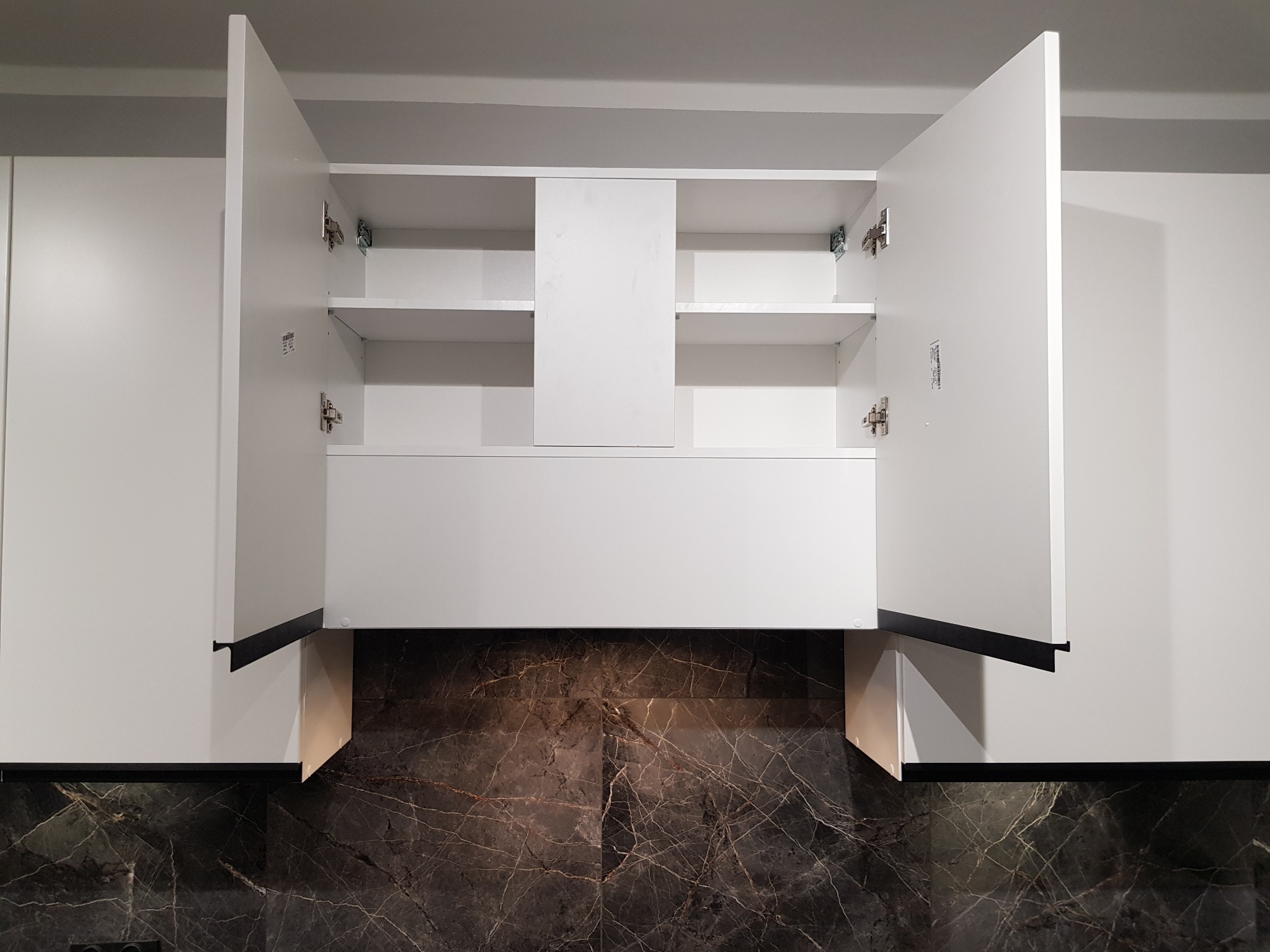Biała szafka kuchenna z otwartymi drzwiczkami, widoczne półki wewnętrzne, czarne uchwyty krawędziowe, marmurowy backsplash podświetlony od dołu.