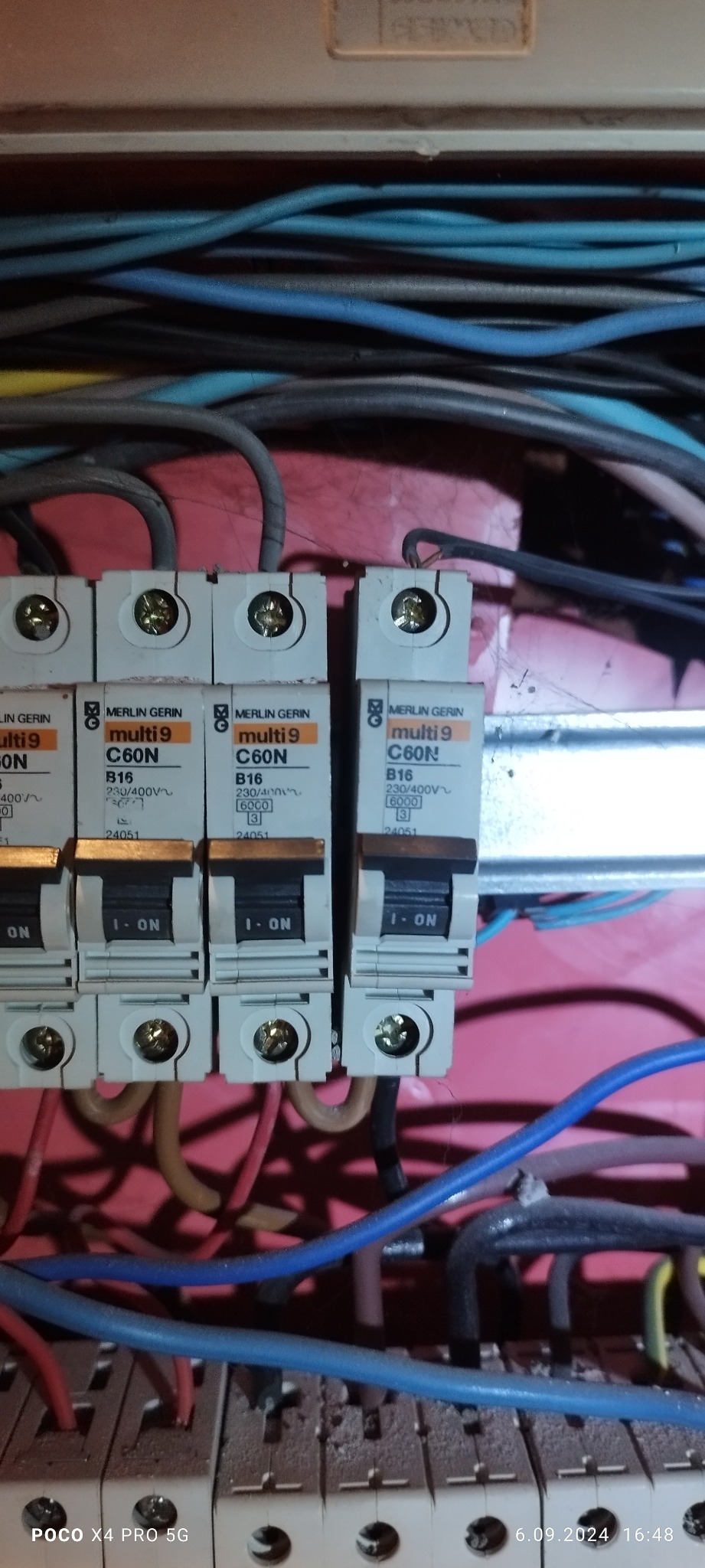 Rozdzielnia elektryczna z czterema bezpiecznikami Merlin Gerin C60N i B16, widoczne przewody w różnych kolorach wewnątrz obudowy.