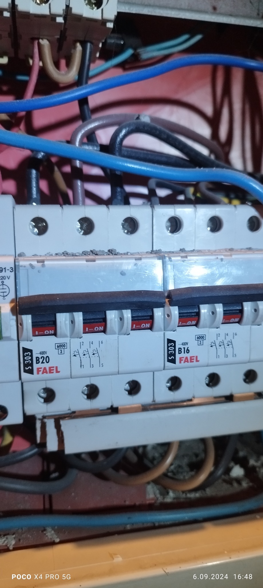 Szczegółowe ujęcie tablicy rozdzielczej z zainstalowanymi bezpiecznikami FAEL S 303 B16 i B20, widoczne przewody w różnych kolorach, osadzone w czerwonej obudowie.