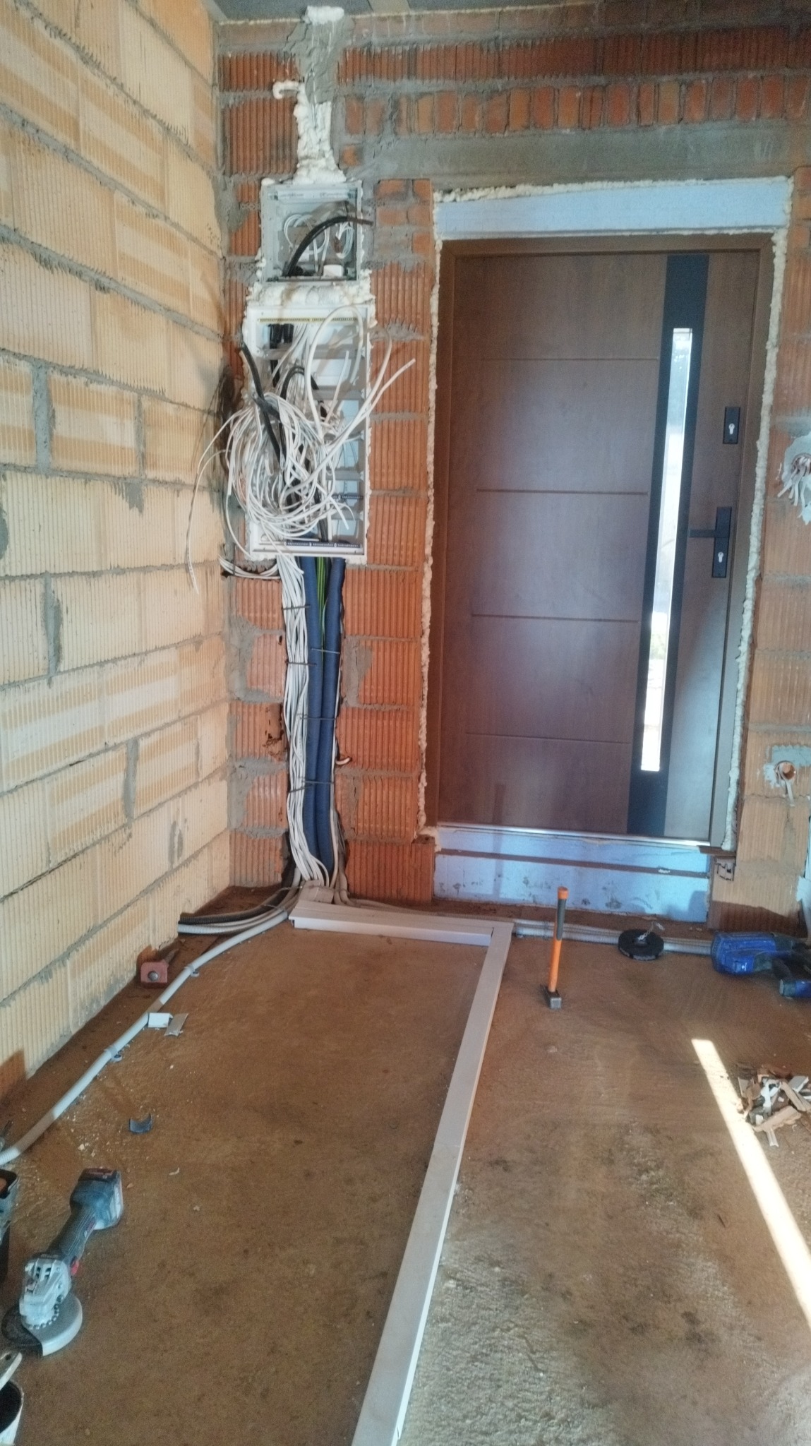 Rozdzielnica z przewodami w surowym wnętrzu, widoczne narzędzia i kable. Instalacja elektryczna w trakcie montażu w nowym budynku z cegły.