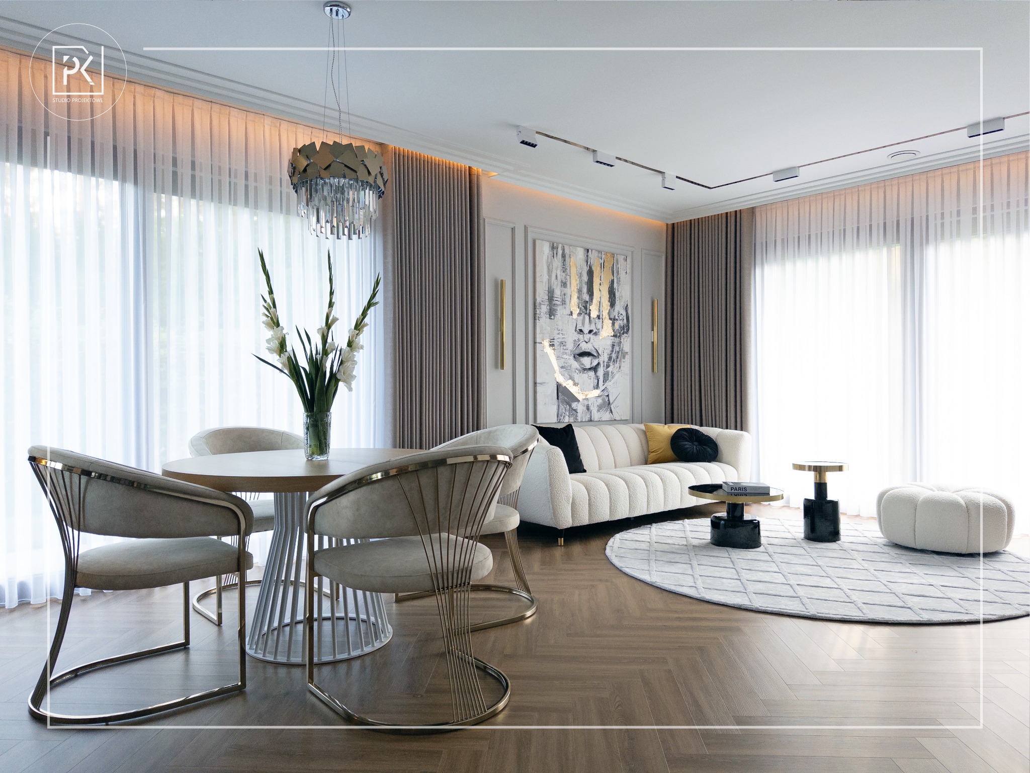 Eleganckie wnętrze salonu z jadalnią: okrągły stół z krzesłami na złotych nogach, biała sofa z poduszkami, okrągły dywan i abstrakcyjny obraz na ścianie, parkiet w jodełkę.