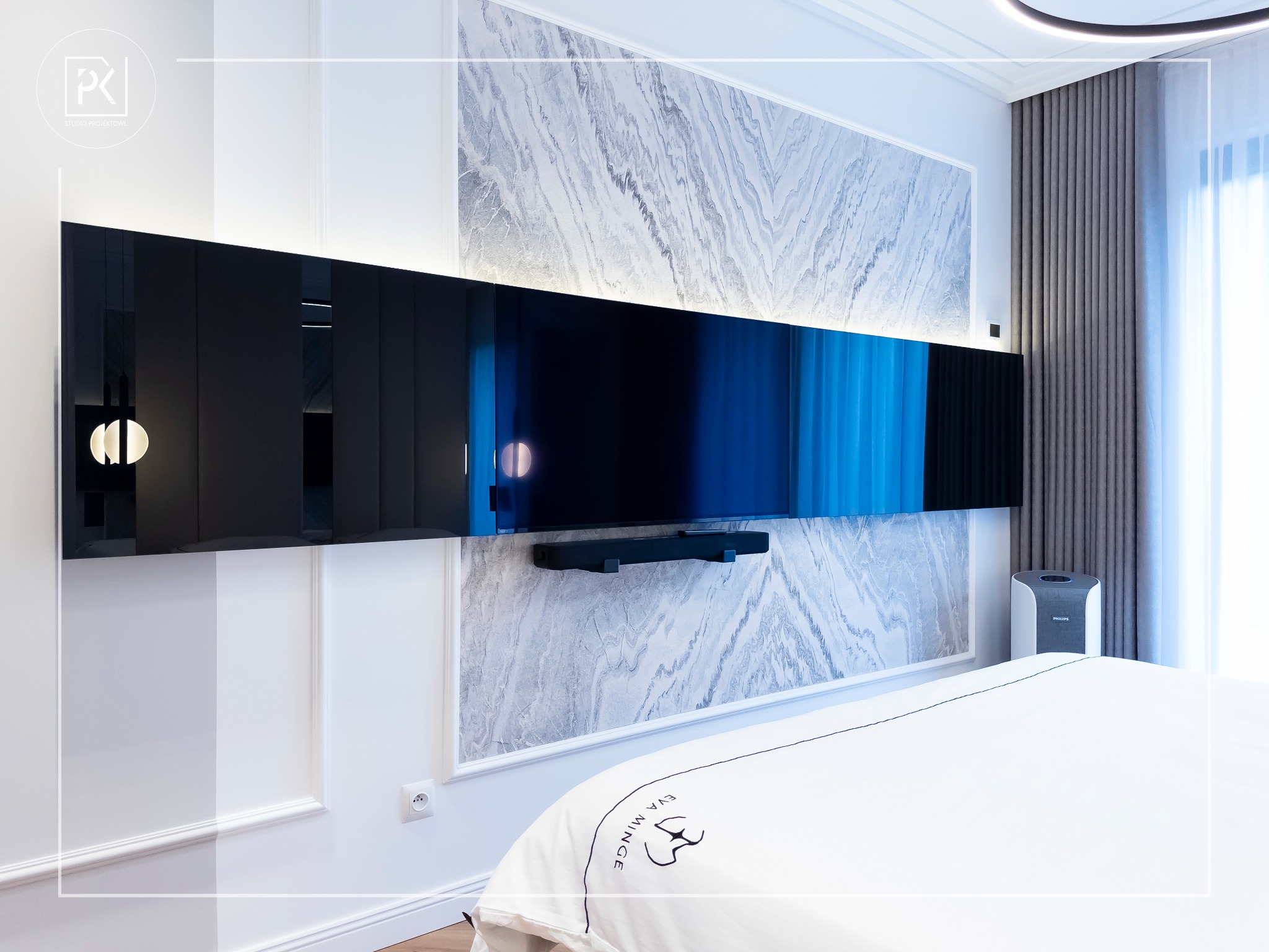 Nowoczesna sypialnia z panelem ściennym imitującym marmur, podświetlonym telewizorem z soundbarem, białą pościelą z logo i oczyszczaczem powietrza Philips.