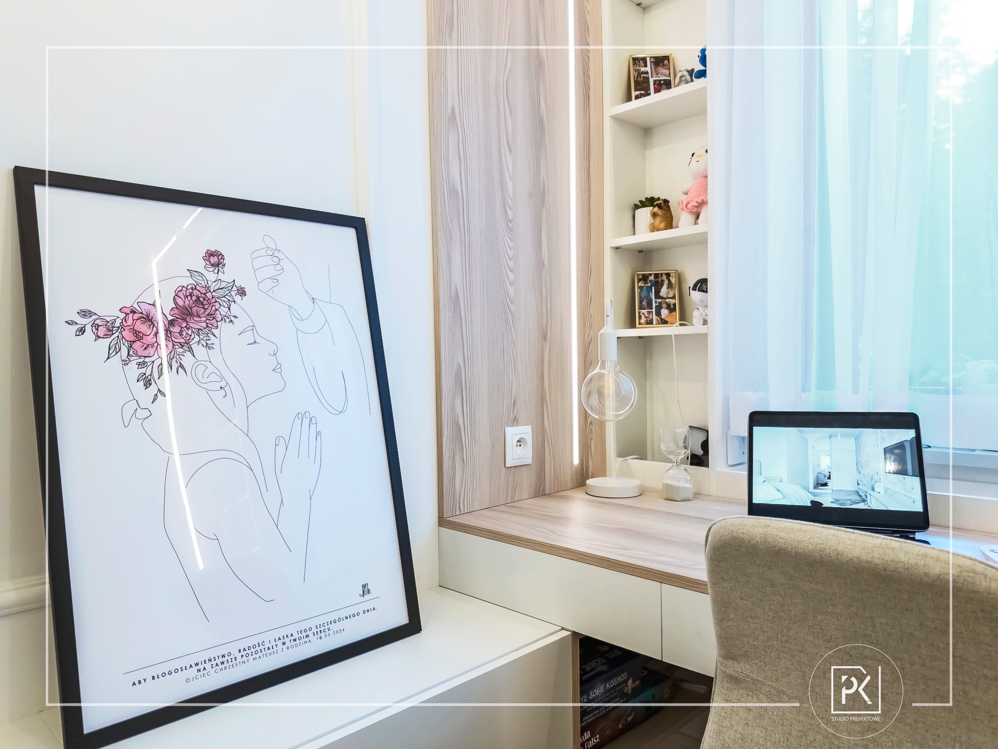 Białe biurko z drewnianym blatem w pokoju, nad nim półki z dekoracjami, na blacie laptop z wizualizacją wnętrza, obok stoi oprawiony plakat z minimalistycznym rysunkiem kobiety z kwiatami we włosach.