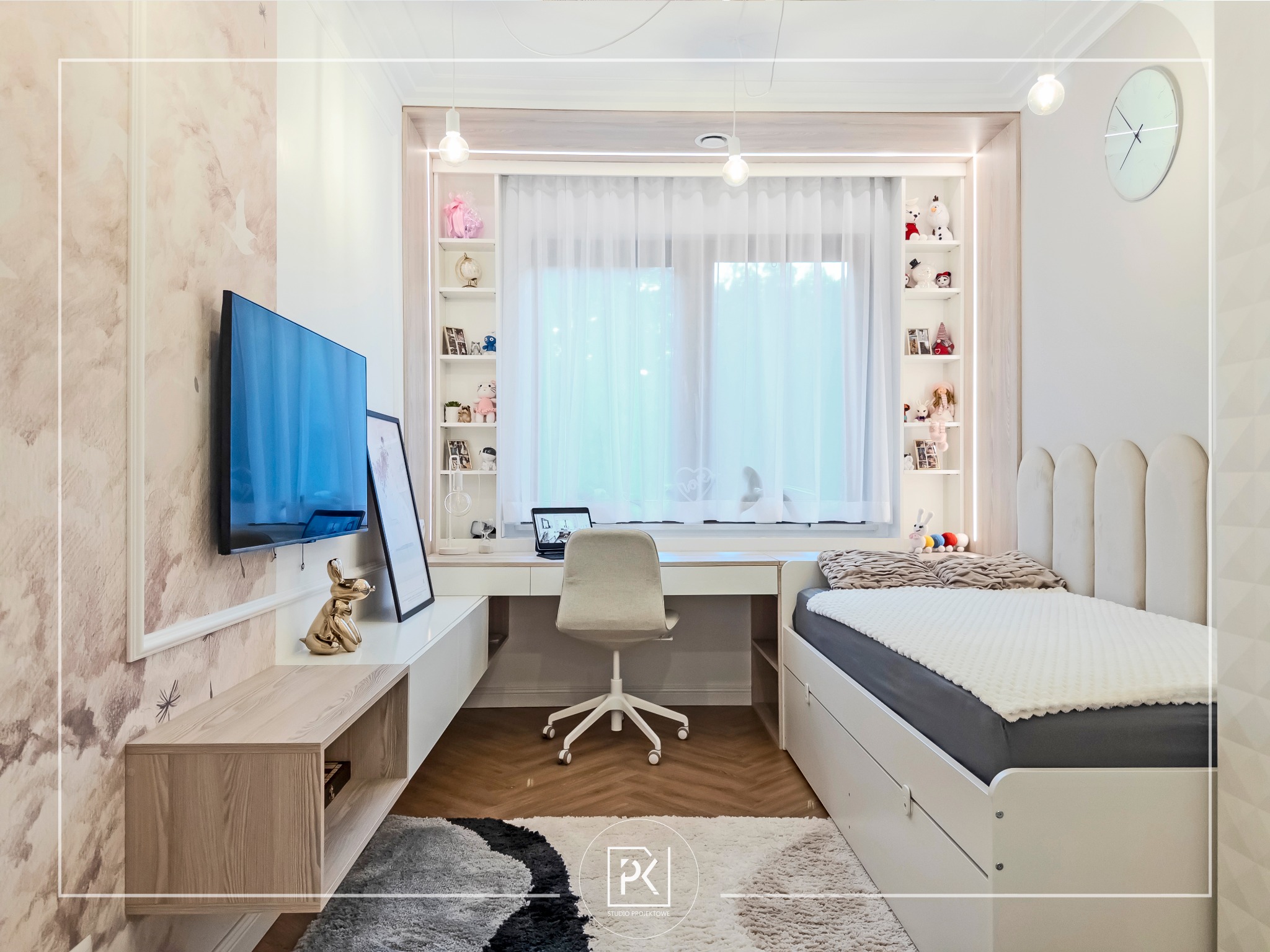 Pokój dziecięcy z łóżkiem z szufladami, biurkiem z półkami, telewizorem na ścianie z tapetą w chmurki, dekoracyjną figurką królika i dywanem w geometryczne wzory.
