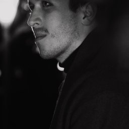 Aureliusz Brzostkiewicz - Czarno-białe portretowe ujęcie z profilu młodego mężczyzny w czarnym golfie, oświetlonego bocznym światłem, z widocznym fragmentem lampy w tle.