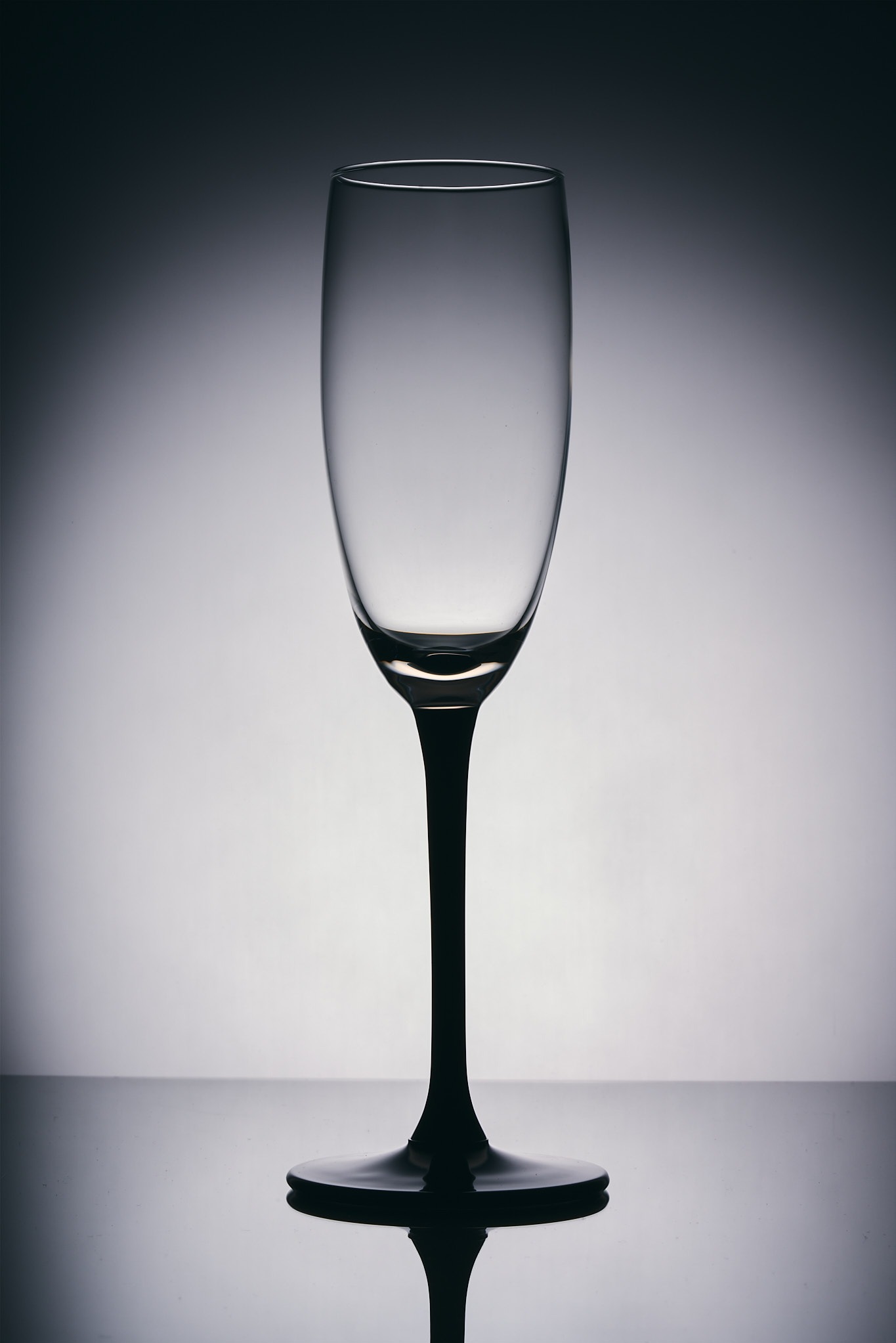 Pusty kieliszek do szampana na wysokiej nóżce, sfotografowany w studiu z gradientowym tłem i odbiciem w błyszczącej powierzchni.