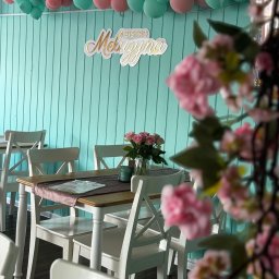 MELUZYNA - Uroczysty wystrój wnętrza bistro z turkusowymi ścianami, balonami w kolorach różu i mięty, stołami z białymi krzesłami, bukietem róż w wazonie i dekoracją kwiatową z przodu