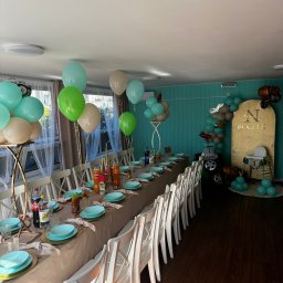 MELUZYNA - Uroczysty stół z turkusową zastawą i dekoracjami z balonów w odcieniach zieleni i beżu, przygotowany na przyjęcie urodzinowe dziecka z motywem samochodów.