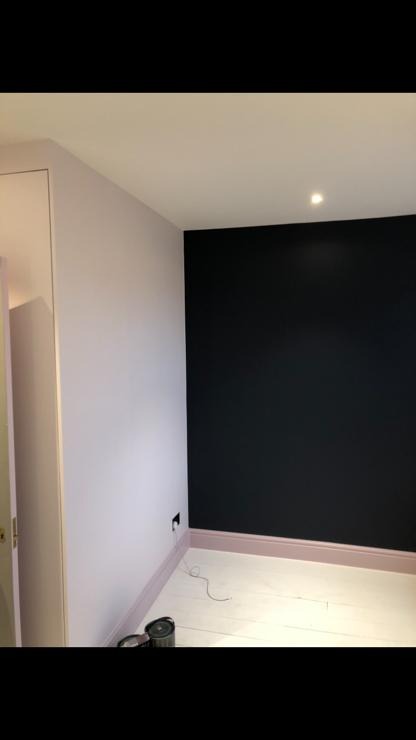 Pokój po odświeżeniu: ściana w kolorze pudrowego różu sąsiaduje z czarną ścianą, listwy przypodłogowe w odcieniu różu, na podłodze leży kabel i puszka farby.