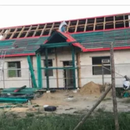 Budowa domu jednorodzinnego w trakcie montażu więźby dachowej i deskowania, widoczne pustaki, niezadaszony ganek, drabina oparta o ścianę, teren budowy z lekkim nieporządkiem.