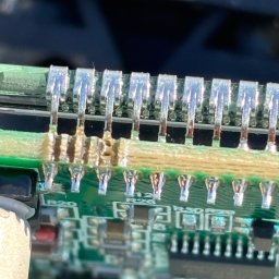 Hubert Bielecki - Zbliżenie na uszkodzone połączenia lutowane na zielonej płytce drukowanej w urządzeniu elektronicznym, widoczne ślady przegrzania i stopionego spoiwa.