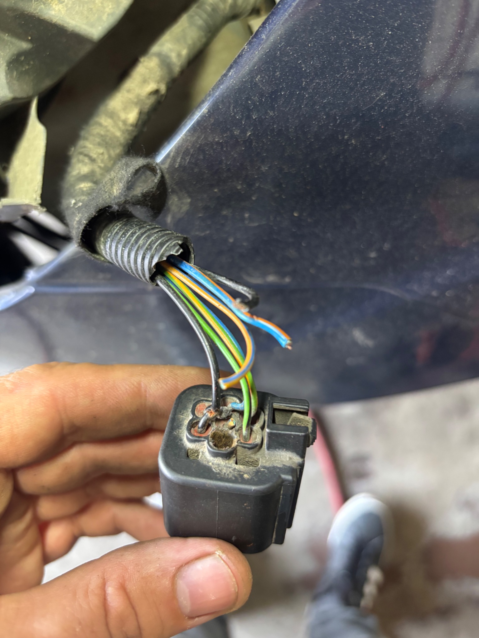 Uszkodzona wiązka elektryczna samochodu z widocznymi przewodami w kolorach: niebieskim, zielonym i pomarańczowym, trzymana w dłoni, z fragmentem nadkola w tle.