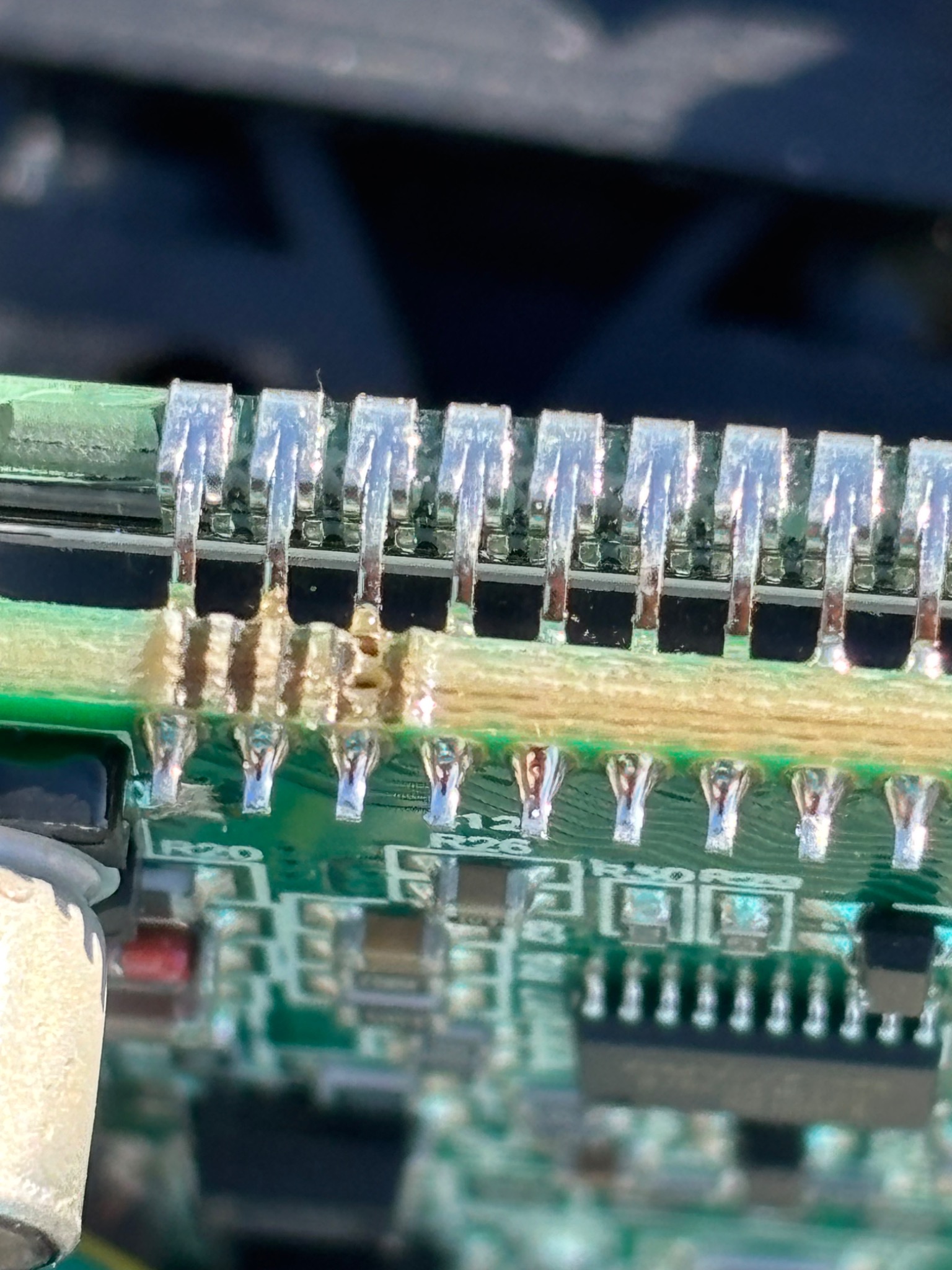 Zbliżenie na uszkodzone połączenia lutowane na zielonej płytce drukowanej w urządzeniu elektronicznym, widoczne ślady przegrzania i stopionego spoiwa.