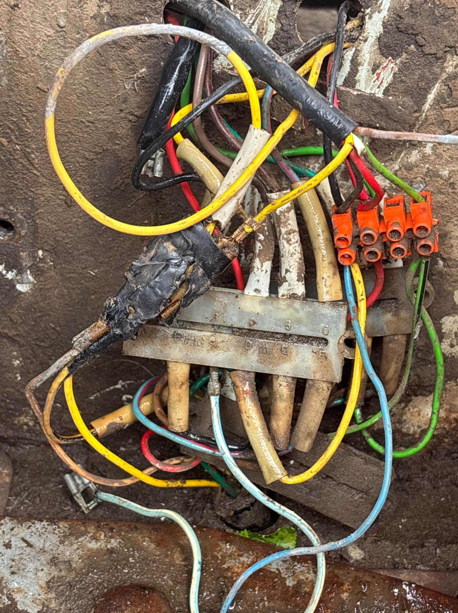 Z bliska widok zanieczyszczonych, starych kabli elektrycznych w różnych kolorach, połączonych za pomocą listwy zaciskowej i izolacji, w brudnym otoczeniu.