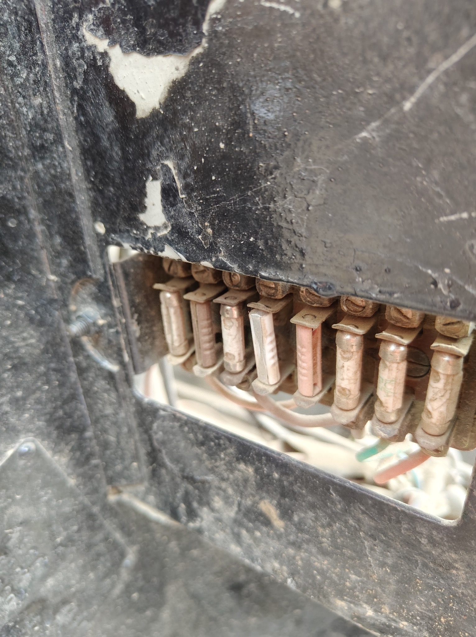 Zbliżenie na skrzynkę z bezpiecznikami samochodowymi, widoczne bezpieczniki topikowe i przewody w brudnej obudowie.