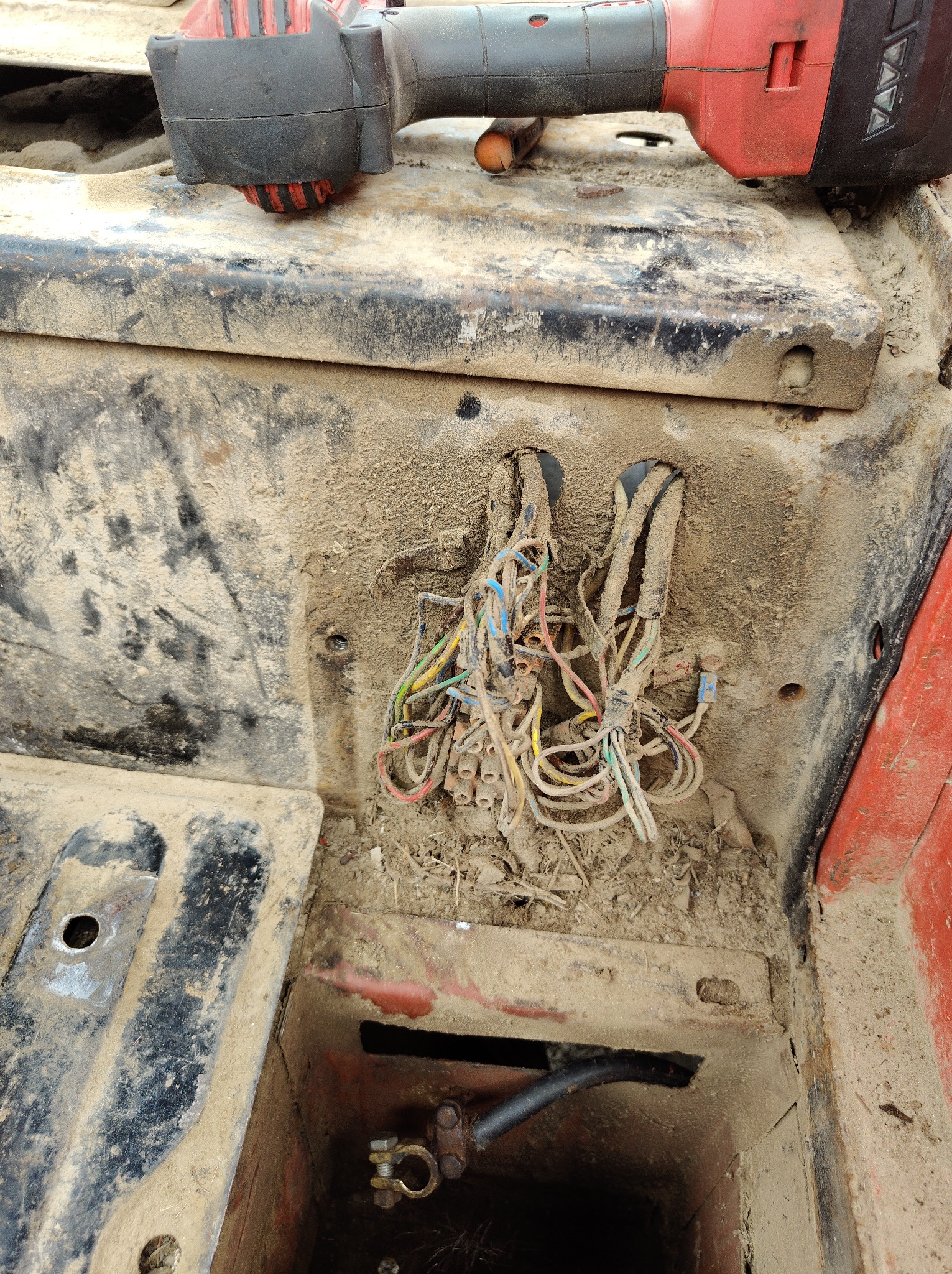 Odkryte, brudne kable elektryczne w pojeździe, z narzędziem akumulatorowym leżącym obok, sugerujące trwające prace naprawcze.