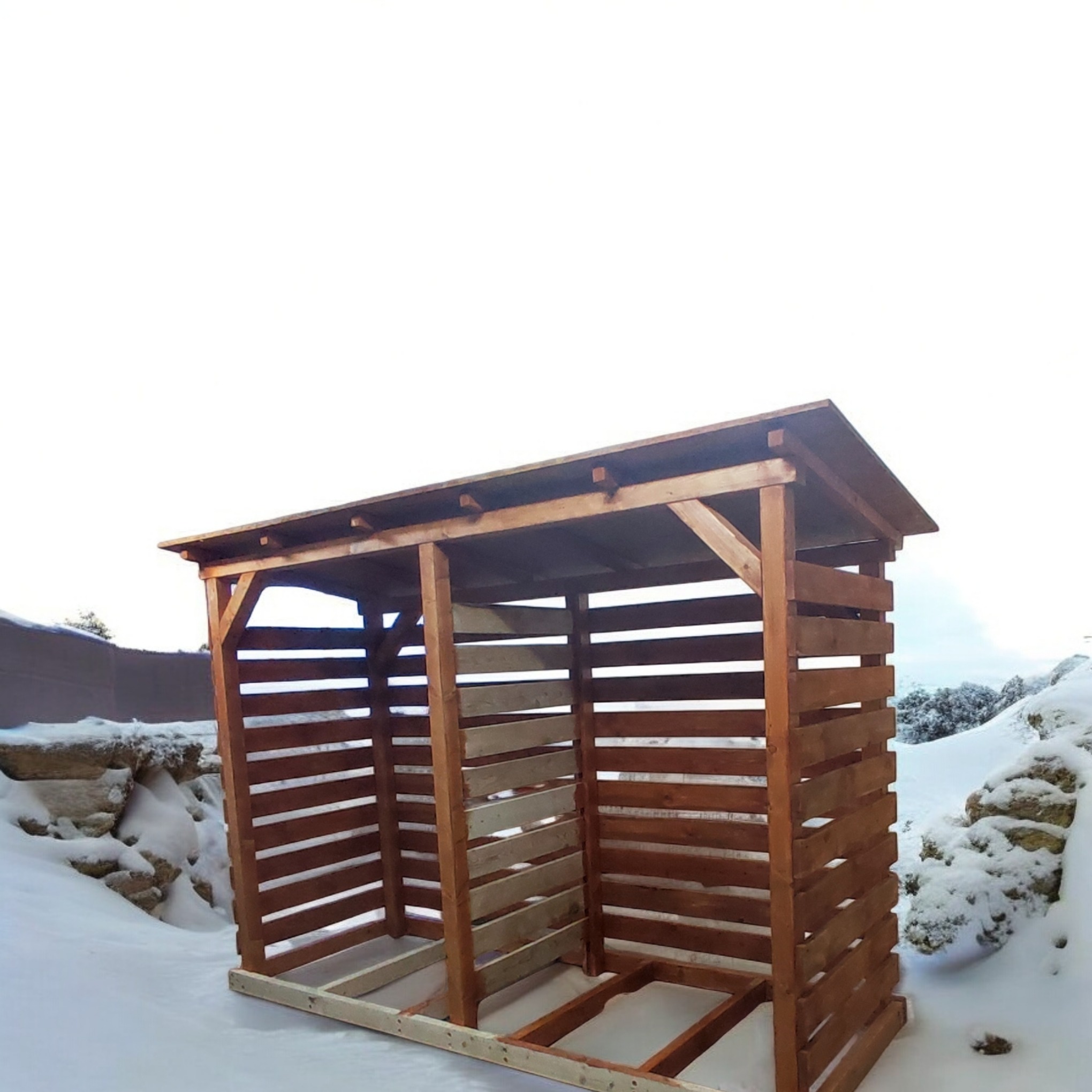 Drewniana konstrukcja w trakcie budowy, prawdopodobnie składzik na drewno opałowe, z widocznymi poziomymi listwami i elementami szkieletu, na tle zimowego krajobrazu ze śniegiem.